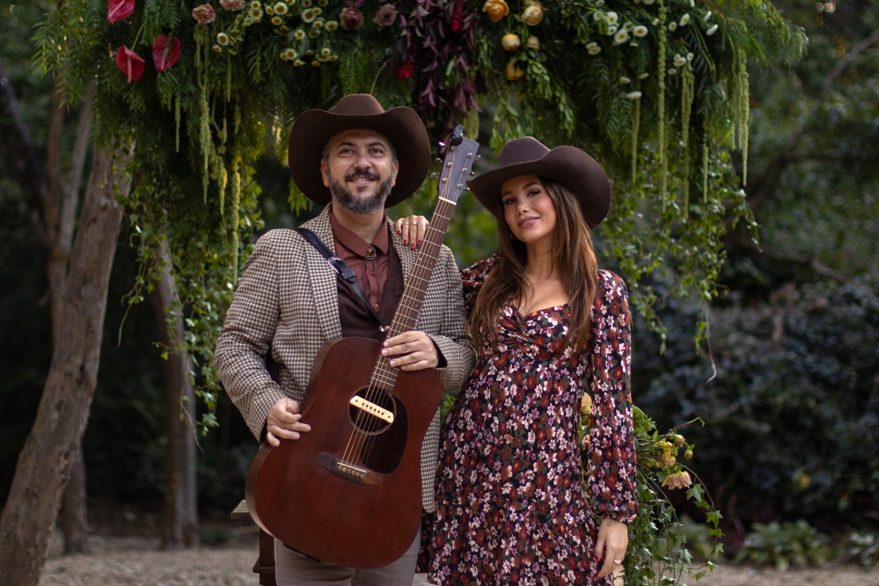 Cantora e violonista de chapéu sob um arco de flores no jardim